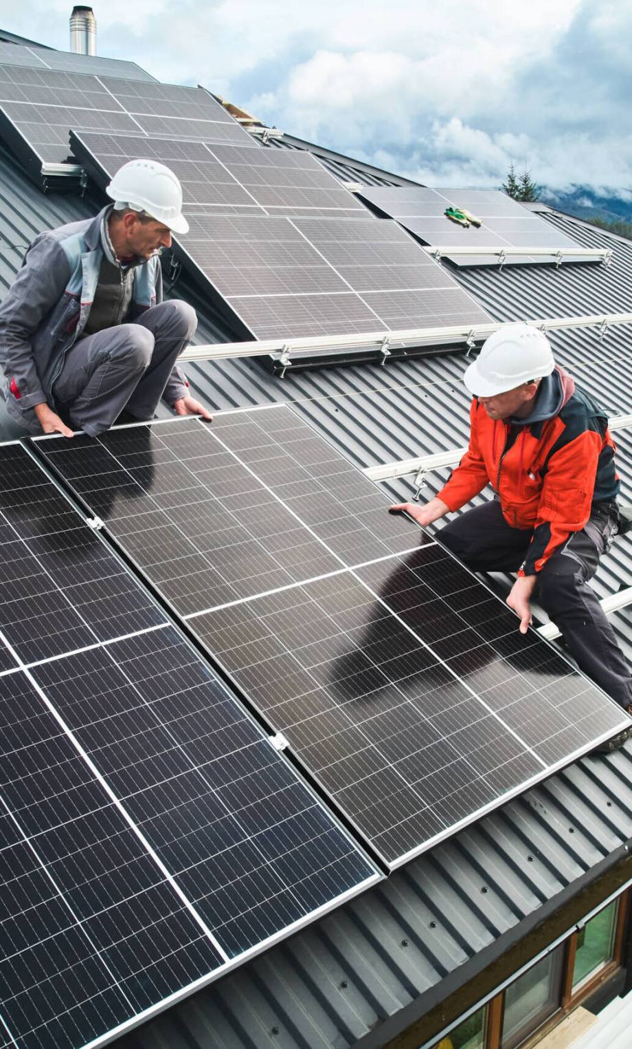 Workers building photovoltaic solar module station on roof of house. Men electricians in helmets installing solar panel system outdoors. Concept of alternative and renewable energy. Aerial view.