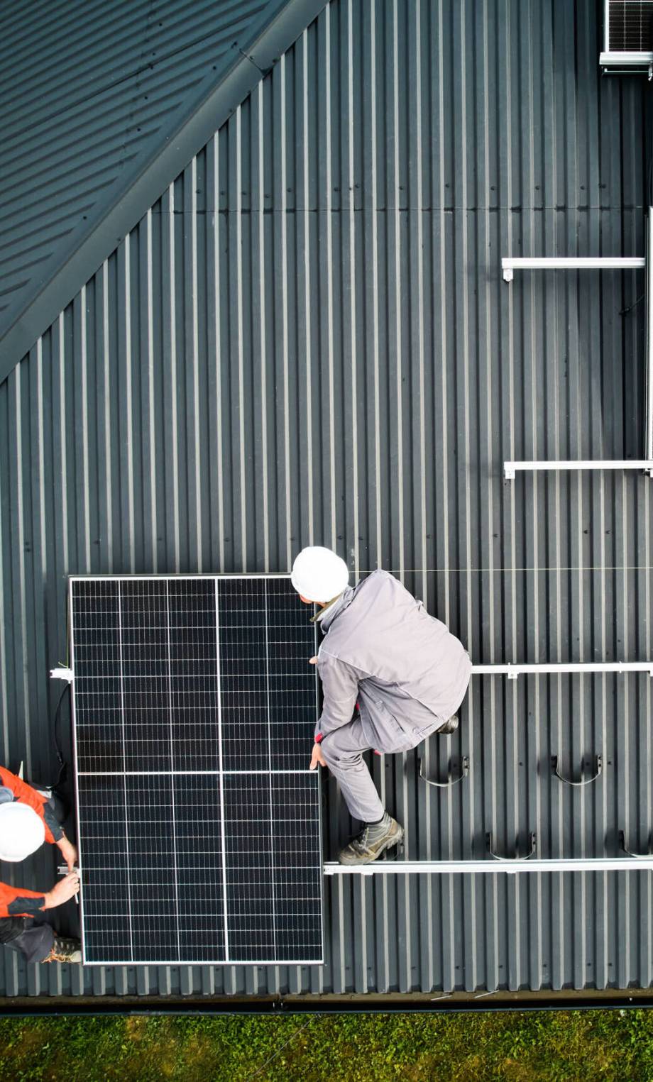 Mounters building photovoltaic solar module station on roof of house. Men electricians in helmets installing solar panel system outdoors. Concept of alternative and renewable energy. Aerial view.